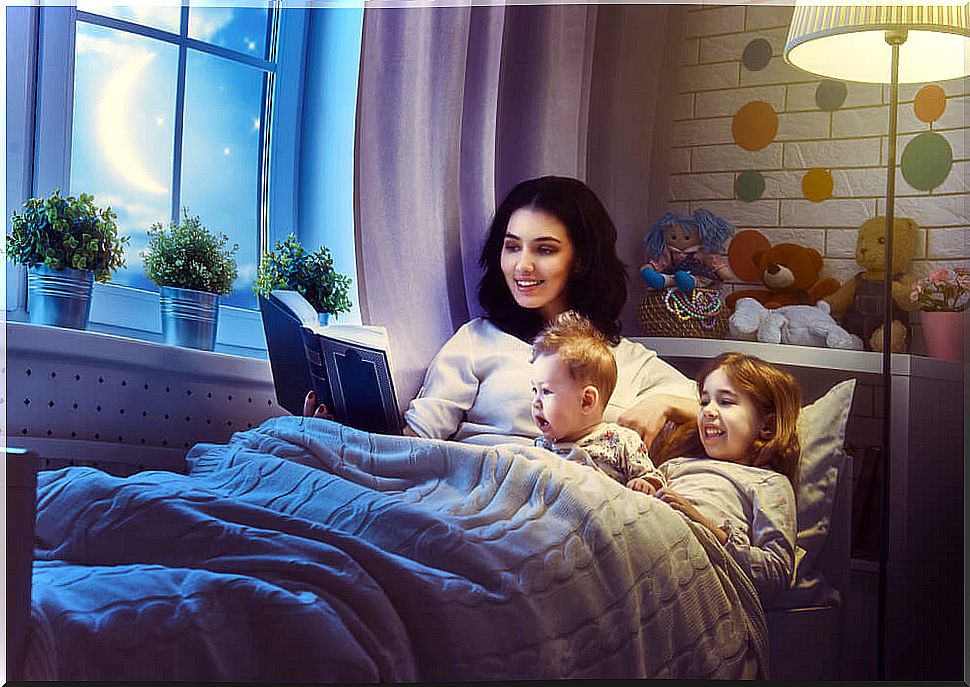 Mother reading modern children's stories to her children in bed.