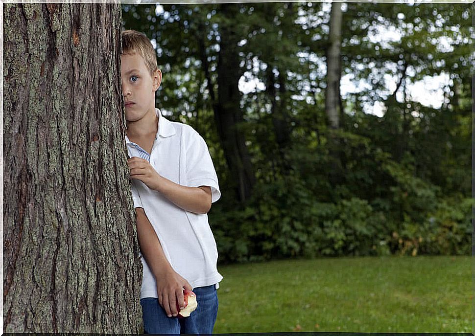 Shy and introverted boy hiding behind a tree who should read some children's books to put shyness aside.