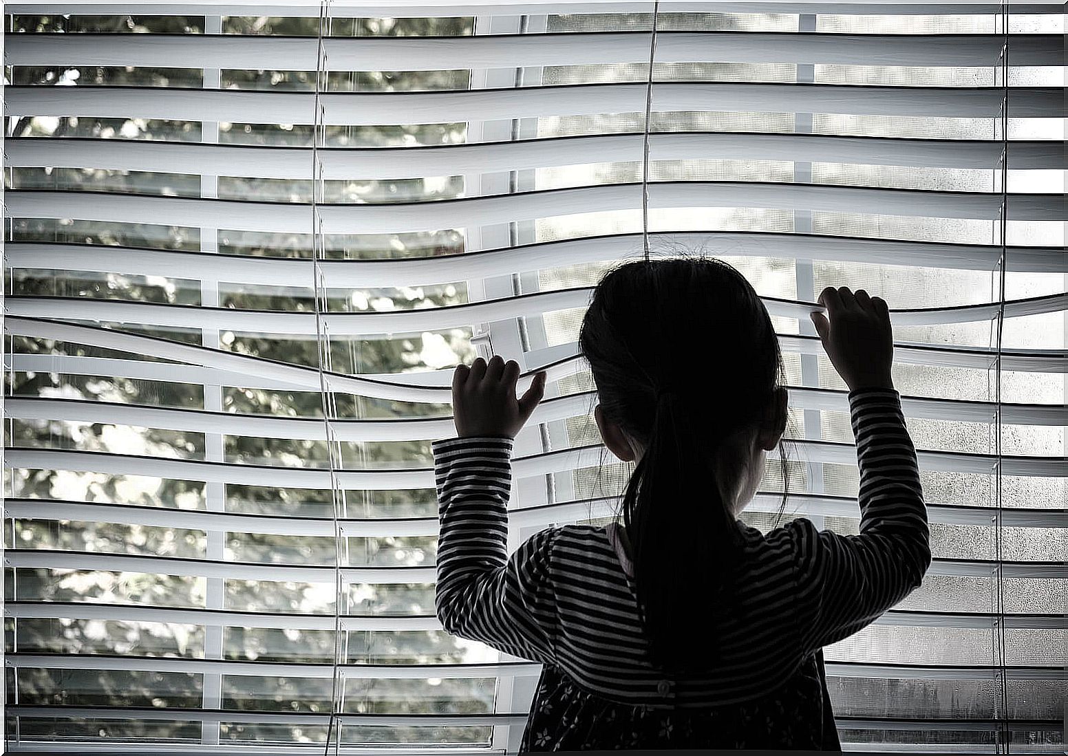 Little girl looking out the window very sad after abandonment, one of the emotional wounds of childhood.