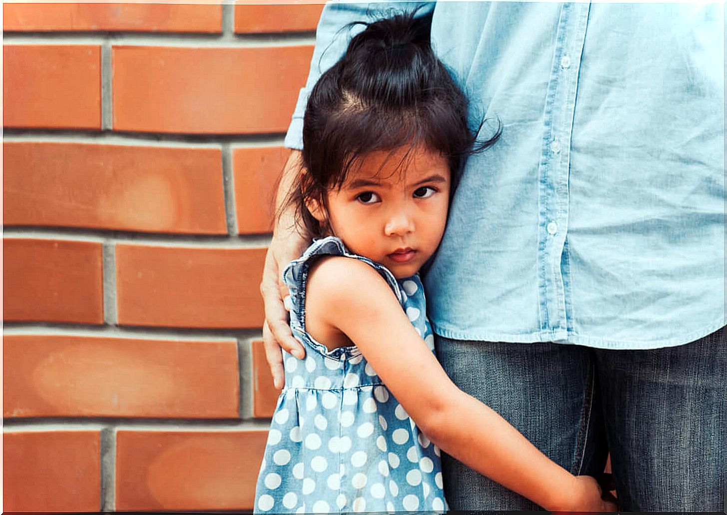 Little girl in fear hugging her father's leg.