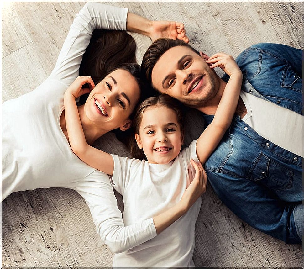 Parents lying next to their daughter on the floor smiling due to the teachings he has provided.